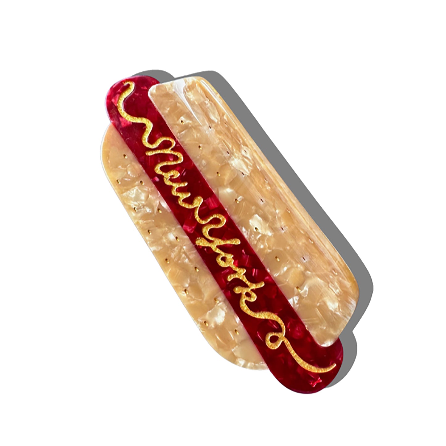 A hot dog-shaped hair claw featuring a marbled beige bun and deep red sausage, finished with gold detailing. The word 'New York' is written in mustard-like script across the top, adding a playful touch. The clip casts a soft shadow against a white background.