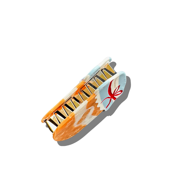 A side view of the peanut butter jar hair claw, showing its strong gold-toned clasp and curved structure. The marbled brown and ivory finish mimics the look of a classic peanut butter jar, while the blue and red accents add a nostalgic touch.