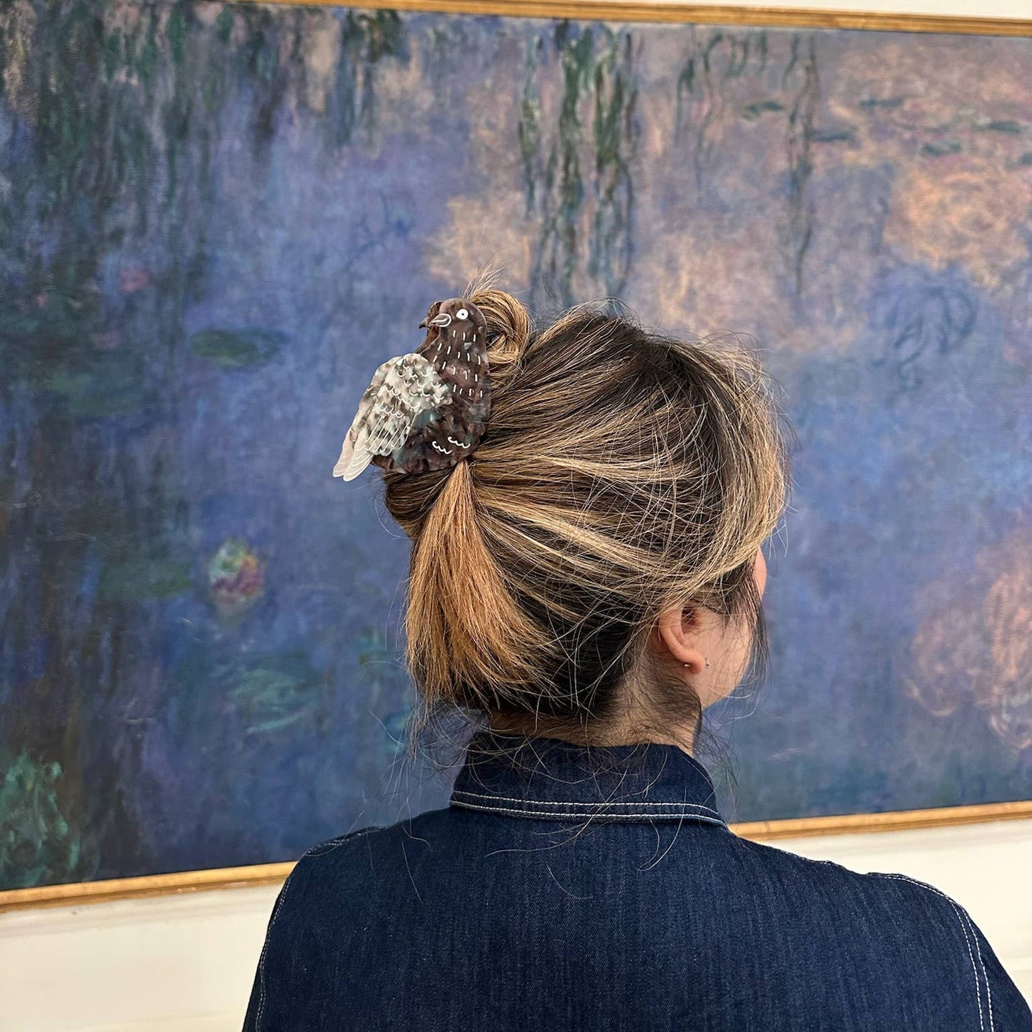 A woman styling the pigeon claw clip in her hair while standing in front of a Monet painting at a museum.