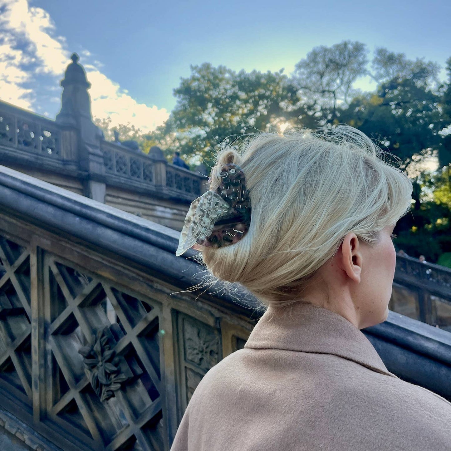 A woman with the pigeon claw clip in a classic twist hairstyle, photographed at an ornate bridge with intricate stone carvings.