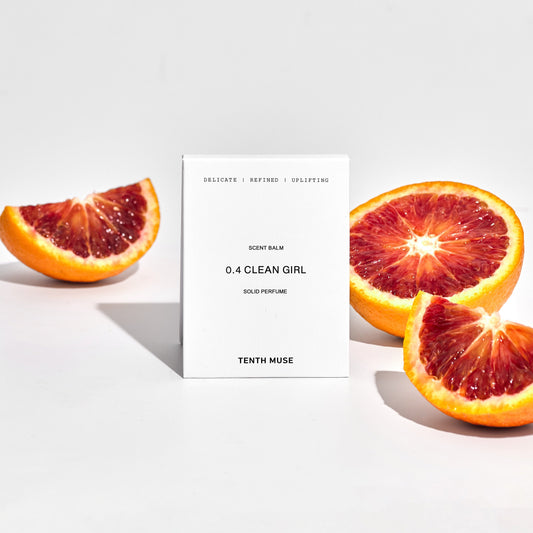 Compact solid perfume balm with the text '0.4 CLEAN GIRL' on it, presented alongside sliced blood oranges.