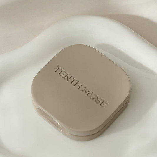 A clay square refillable compact for the tenth muse solid perfume balms. The compact is sitting on top of a white tray and has 'TENTH MUSE' lightly carved into the compact.