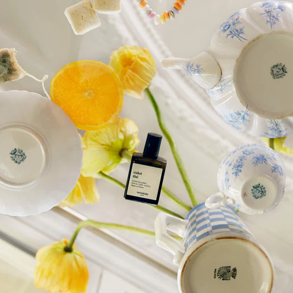Teacups, a bottle of perfume, and flowers on a white surface