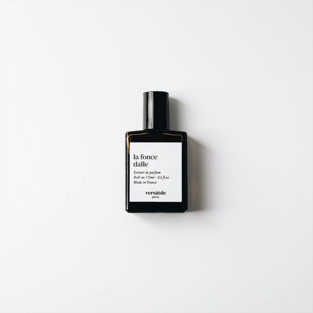 A brown glass bottle on a white background. The lid is black and the label is white with black writing to describe the perfume.