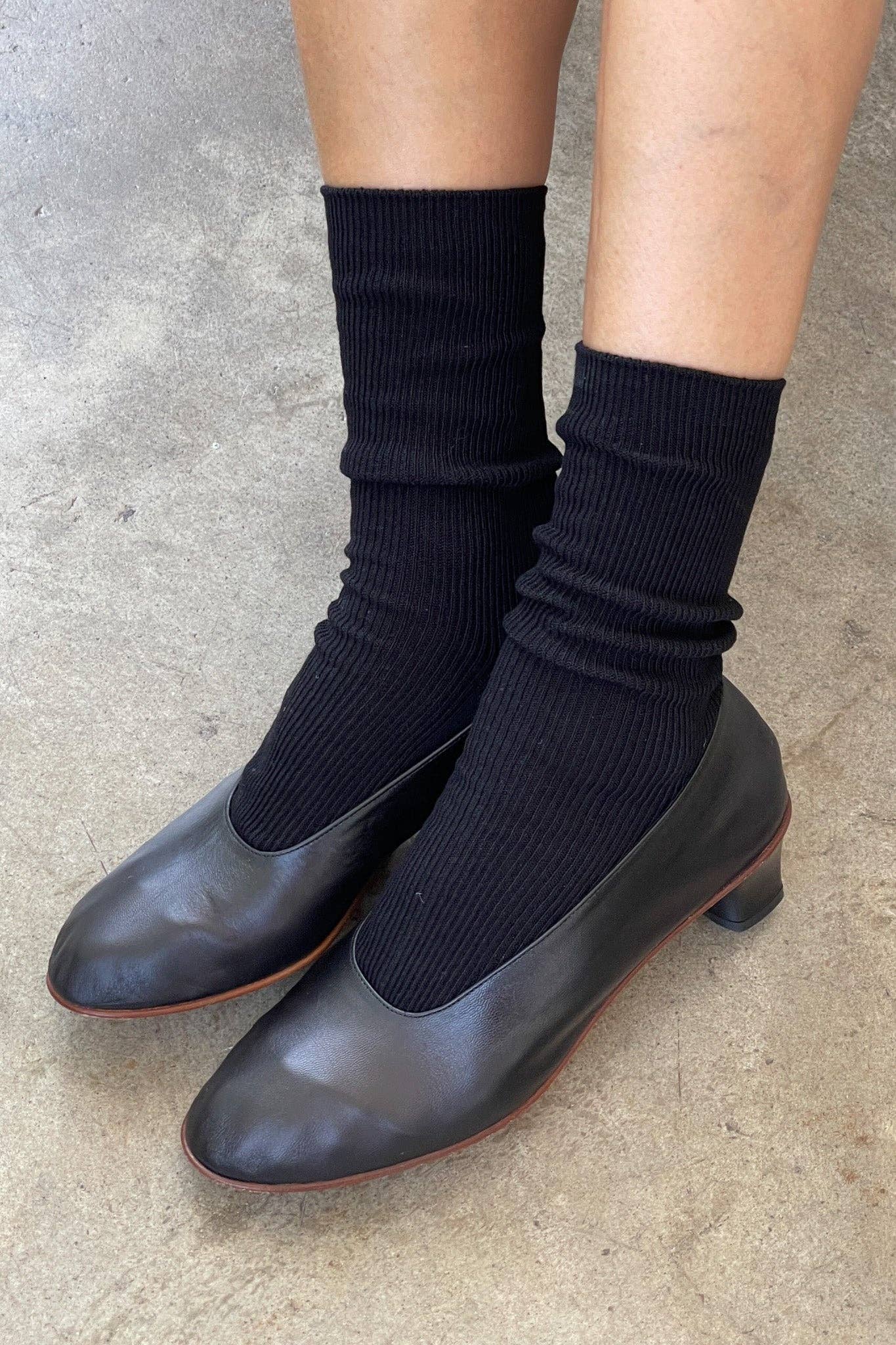 Black socks worn with black shoes on a concrete floor
