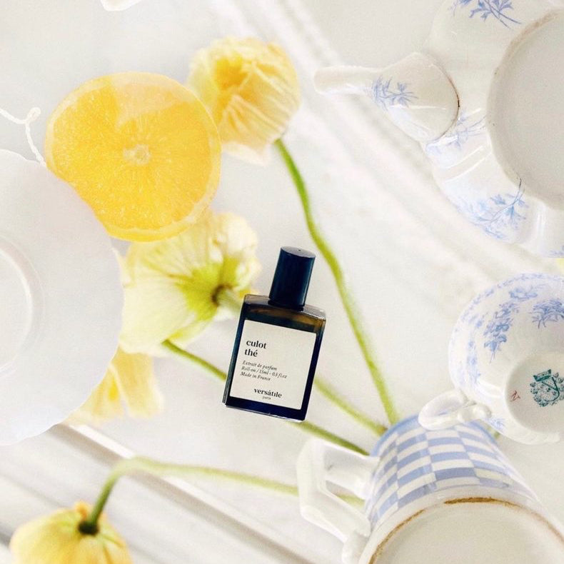 Perfume bottle with yellow flowers and a mug on a white surface