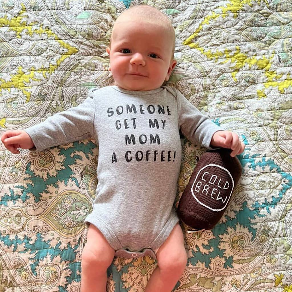 Baby wearing a onesie with text and holding a toy on a patterned surface