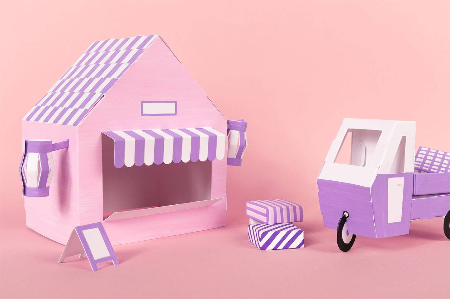 Pink and purple toy house with striped awning and matching car on a pink background