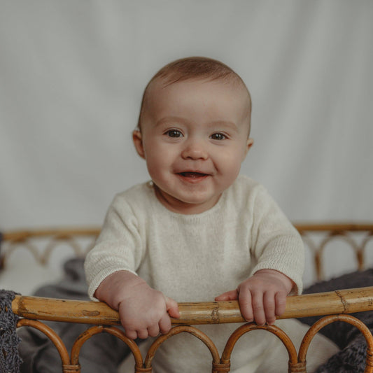 Baby leaning on a wicker crib with a neutral background