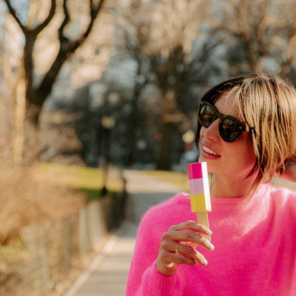 Person in a pink sweater holding a colorful object outdoors with trees in the background