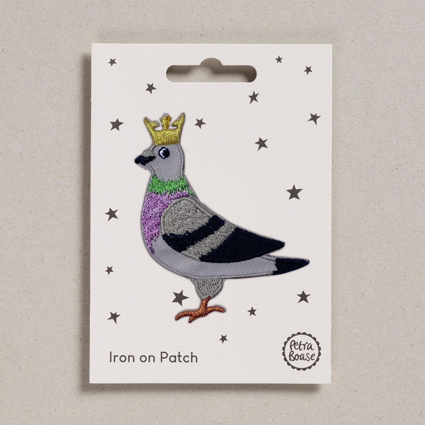 Iron on patch of a pigeon with a crown on a white card with star patterns, branded 'Petra Boase'.
