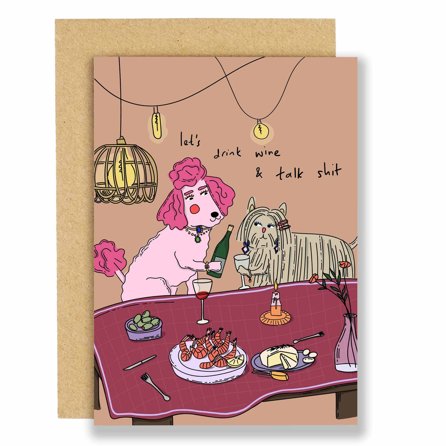 A greeting card with an illustration of two cartoon dogs sitting at a table with wine glasses and a cheese platter, with text that reads 'let's drink wine & talk shit'. The card is designed with a pink and beige color scheme and includes a brown Kraft envelope.