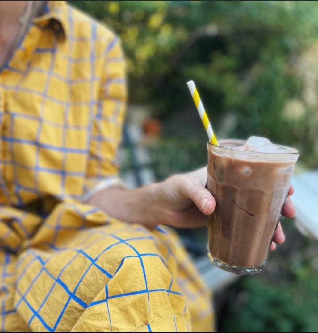 Person holding a glass of chocolate milkshake with a straw outdoors