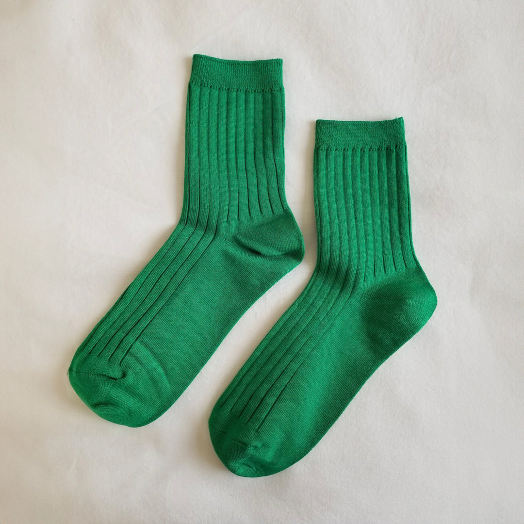 A pair of Kelly green ribbed crew socks laid flat on a white fabric background, showing their full length and texture.