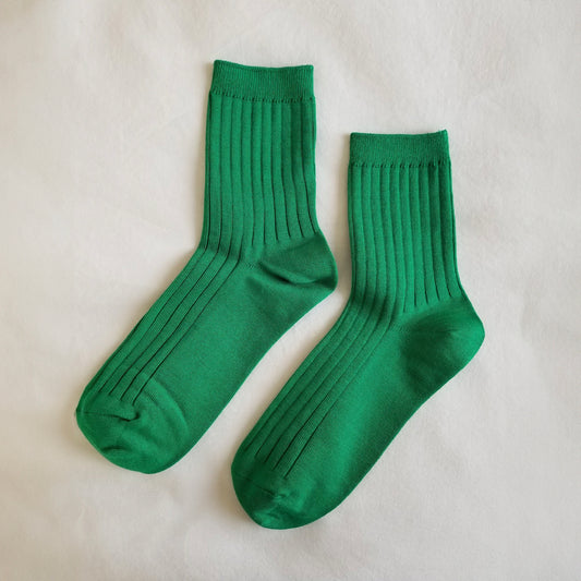 A pair of Kelly green ribbed crew socks laid flat on a white fabric background, showing their full length and texture.
