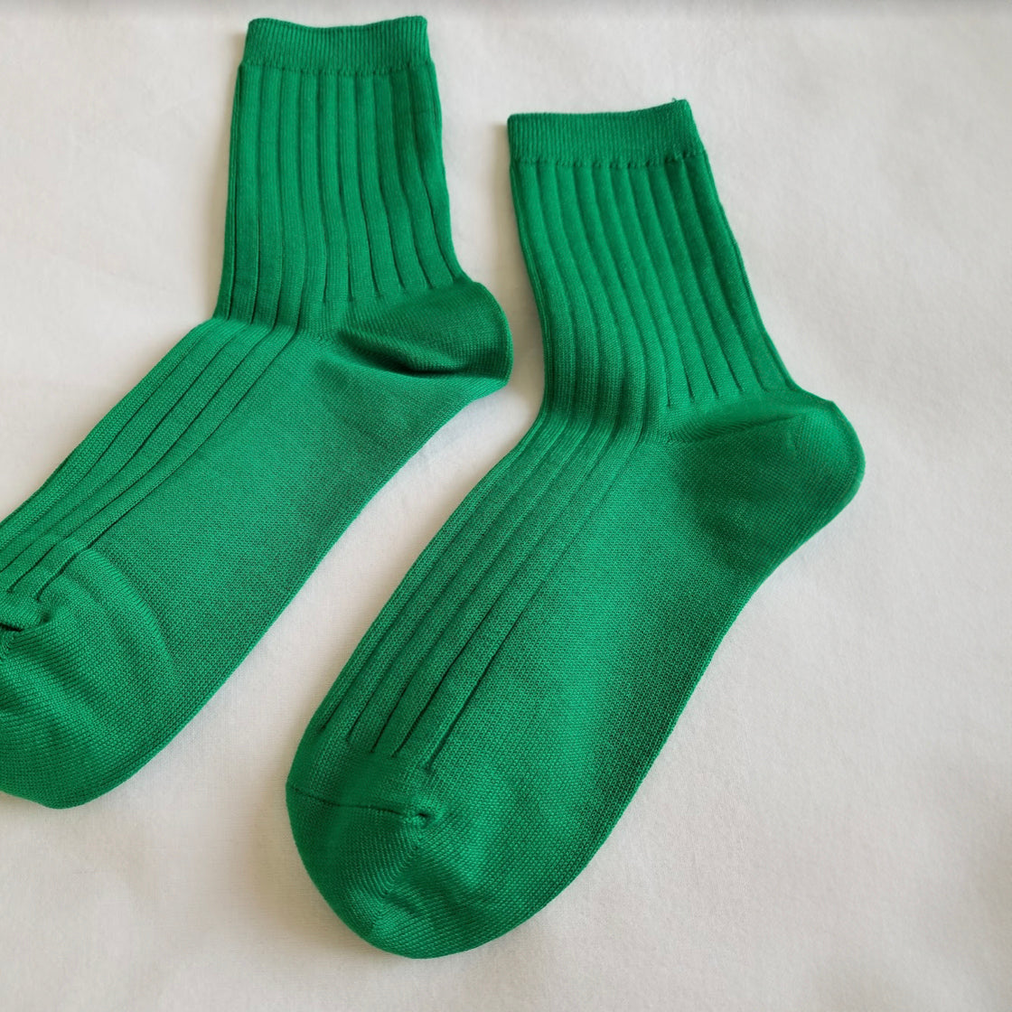 A close-up of Kelly green ribbed crew socks laid flat on a white fabric background, highlighting the ribbed knit texture and soft material.