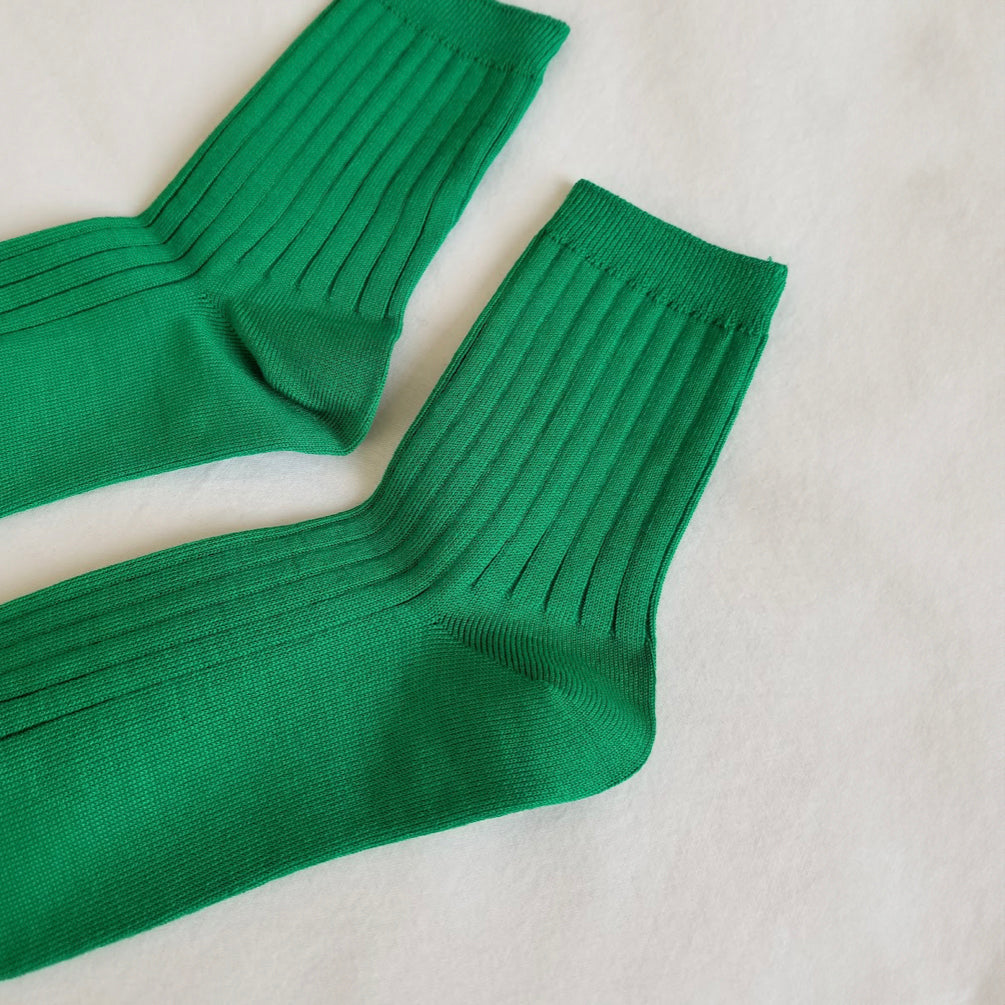 A detailed angled shot of Kelly green ribbed crew socks on a white fabric background, focusing on the toe, heel, and ribbed structure.