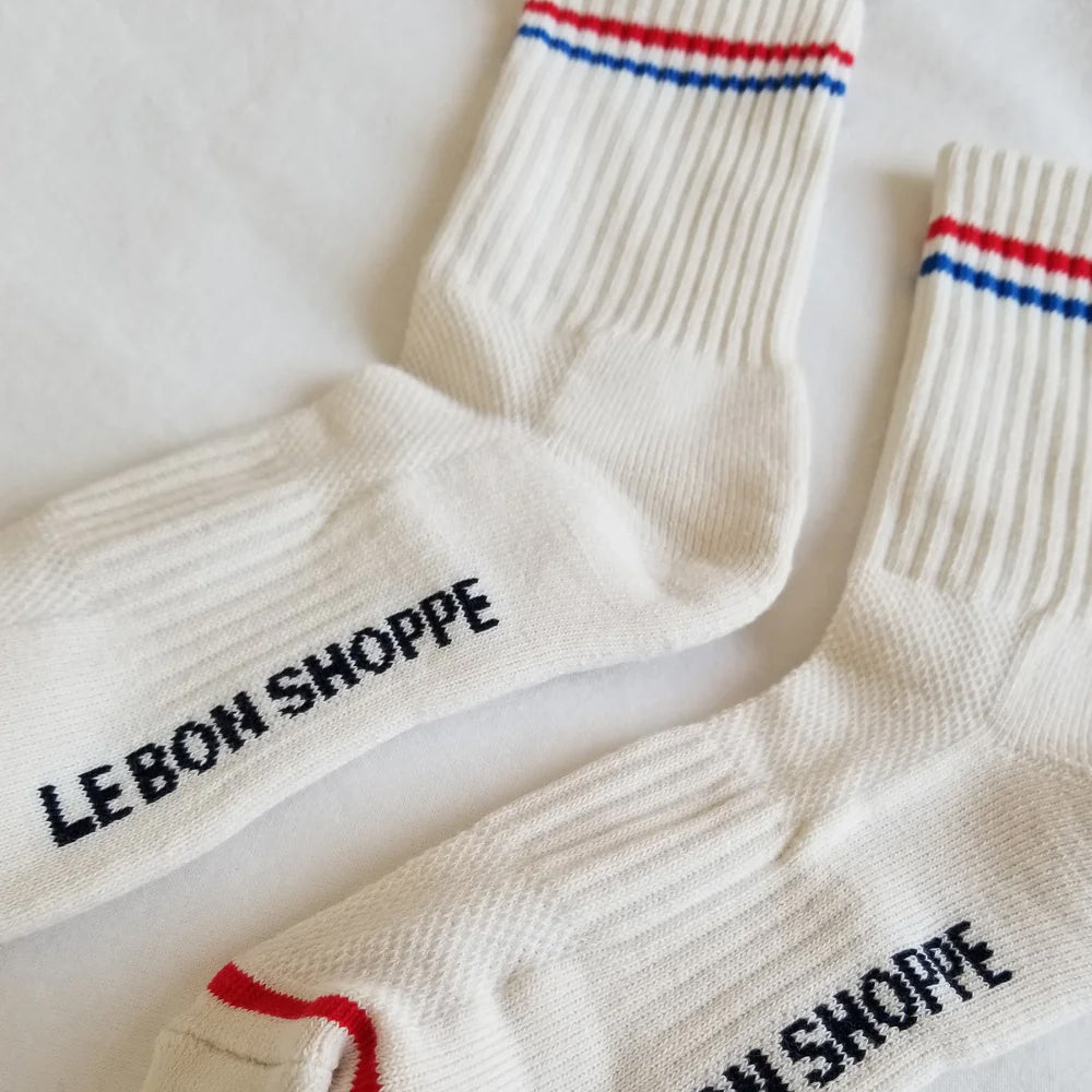 Close-up of cream Le Bon Shoppe Boyfriend Socks with red and blue striped cuffs and logo detail on the sole.