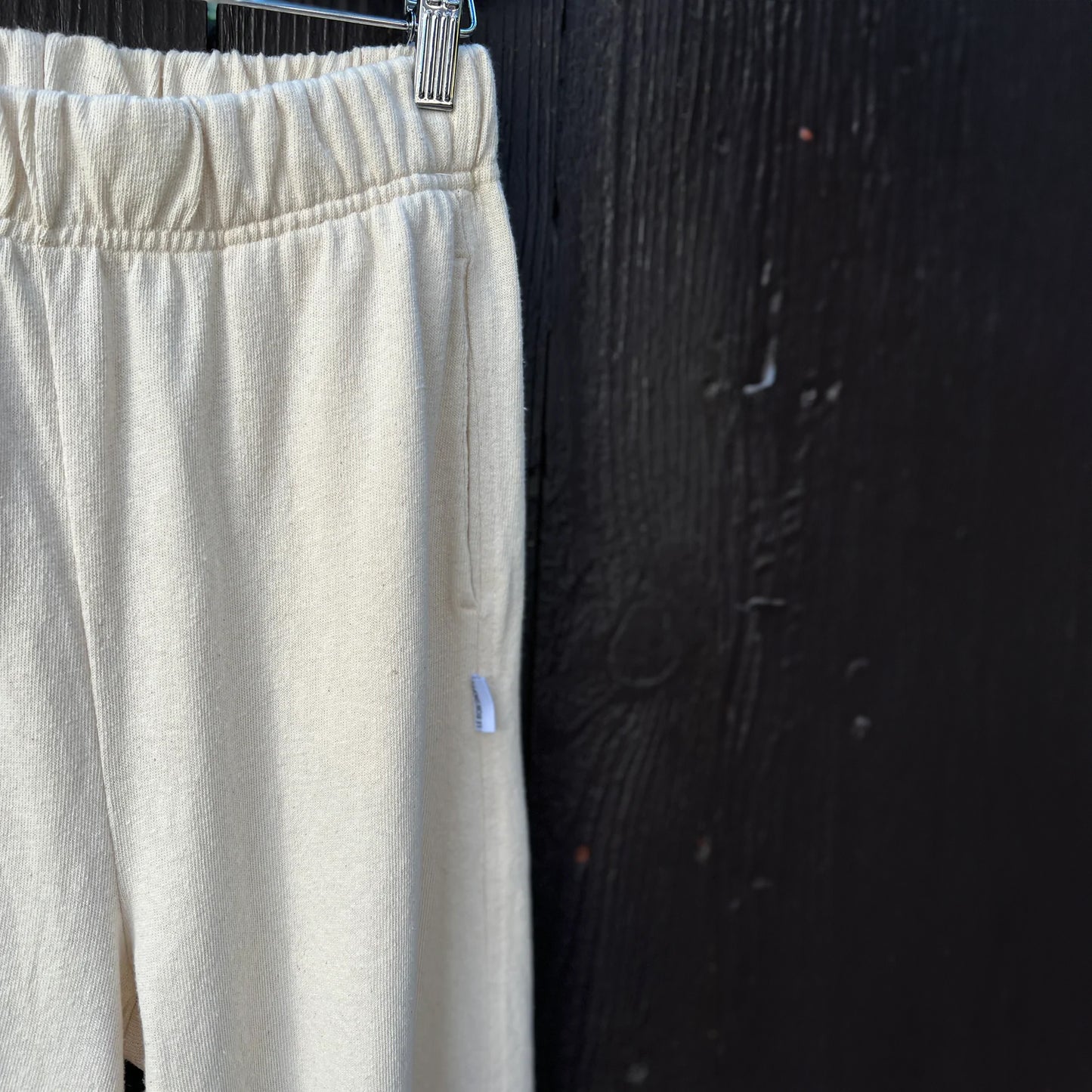 Close-up of Balloon Pants waistband against a black wooden wall – Elastic waist detail with a visible brand tag, showcasing the fabric texture and quality stitching.