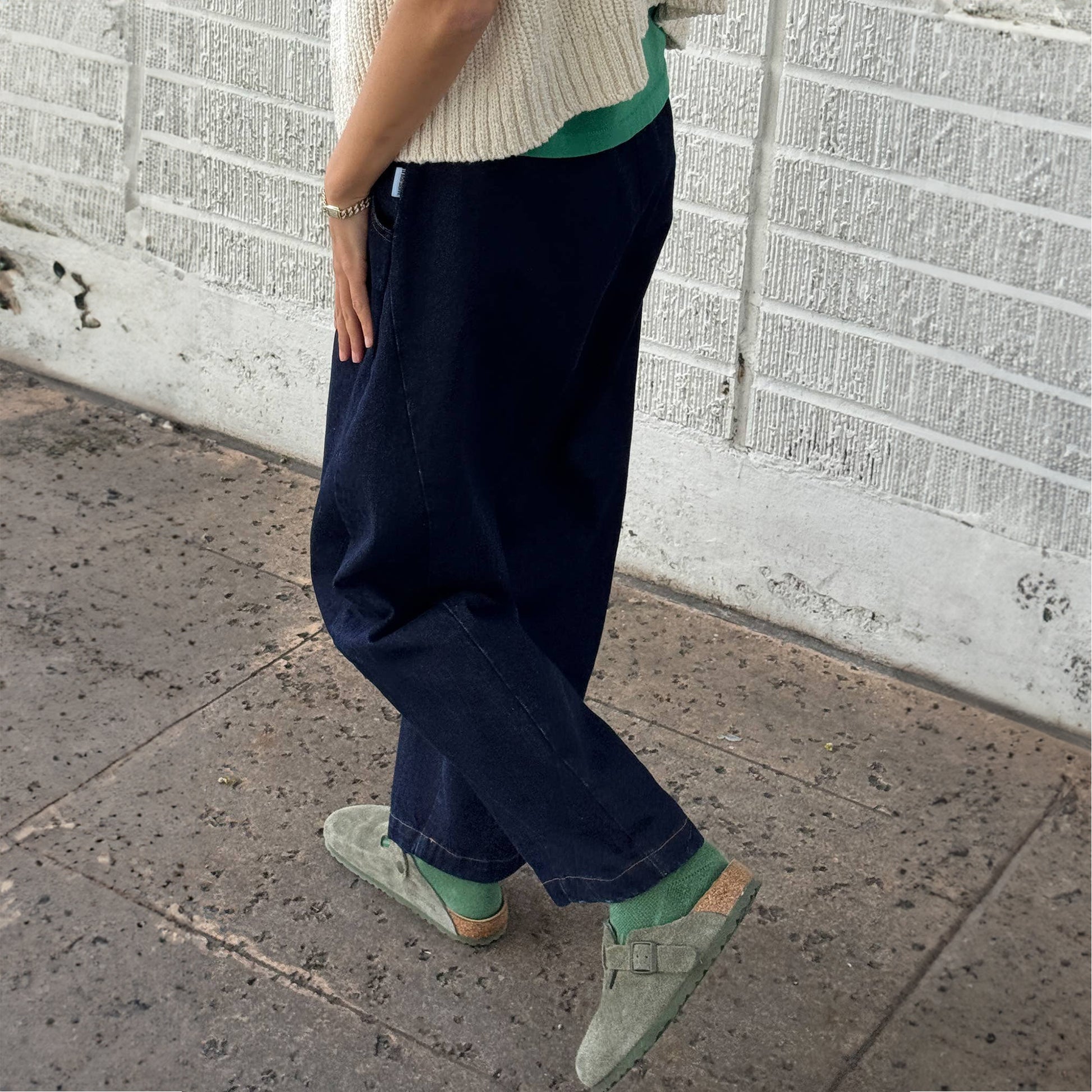 Side view of Arc Pants in Raw Denim styled casually – Worn with green socks and suede Birkenstocks, highlighting the relaxed drape and slightly cropped length.