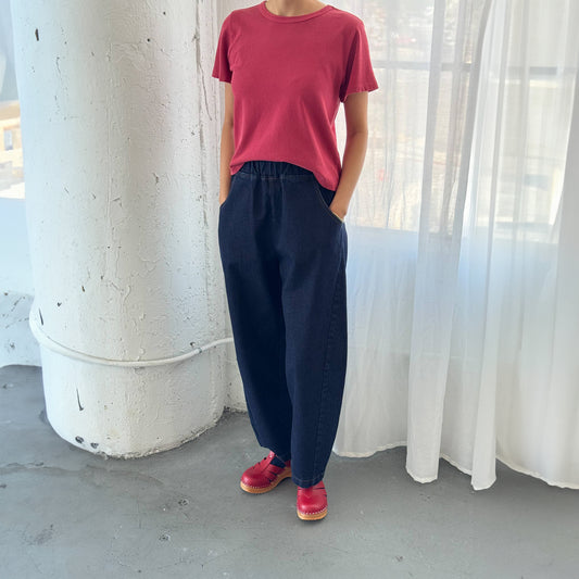 Arc Pants in Raw Denim paired with a red tee and clogs – Styled with a tucked-in tee and bold red shoes for a modern, effortless look, photographed in a bright industrial space.