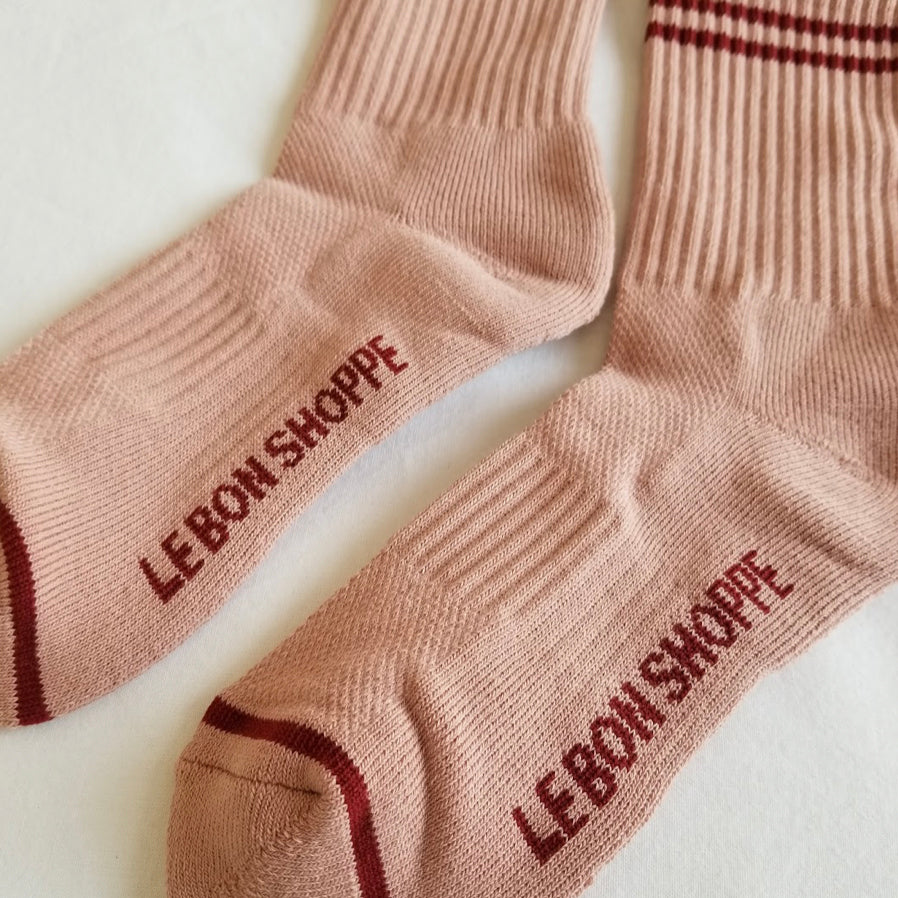 A zoomed-in view of the vintage pink ribbed crew socks, focusing on the "Le Bon Shoppe" branding on the sole, ribbed knit texture, and contrast stripe details.