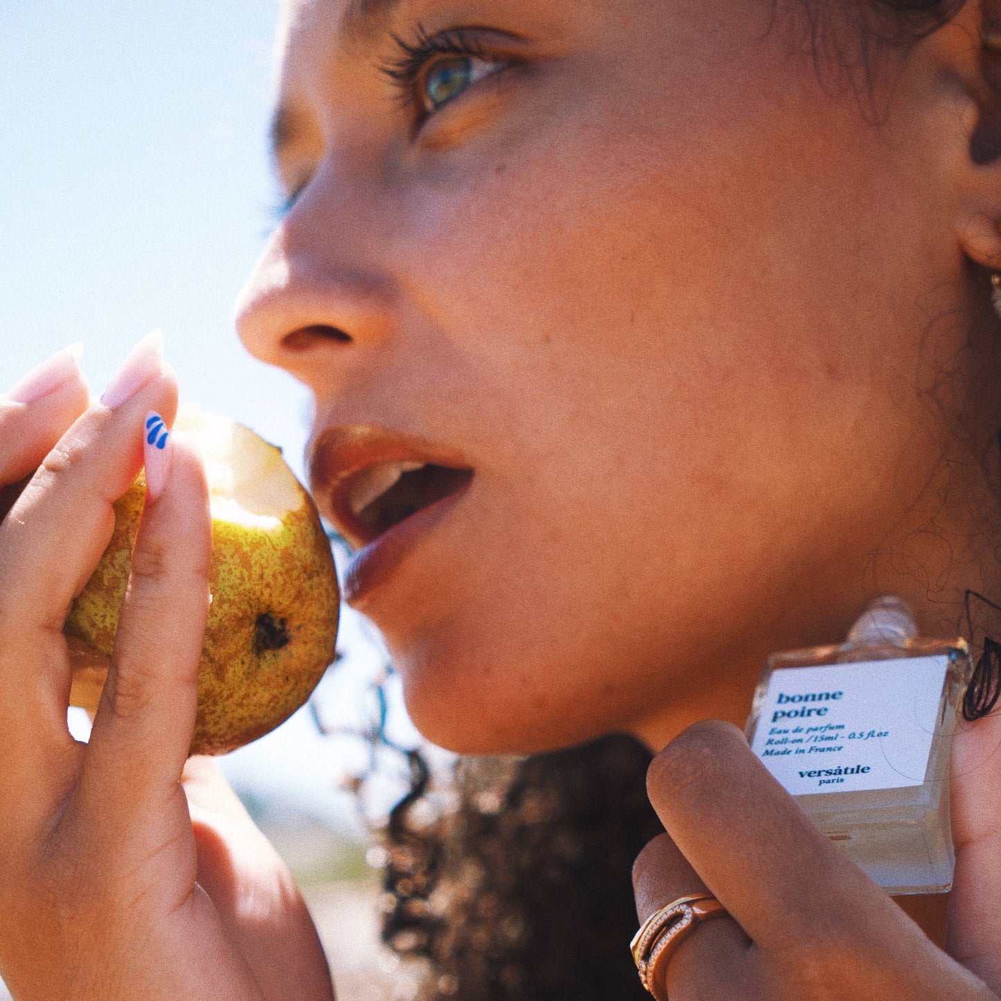 A person is wearing a green top and applying an eau de parfum roll-on to their neck. The product's packaging is visible and has text on it.