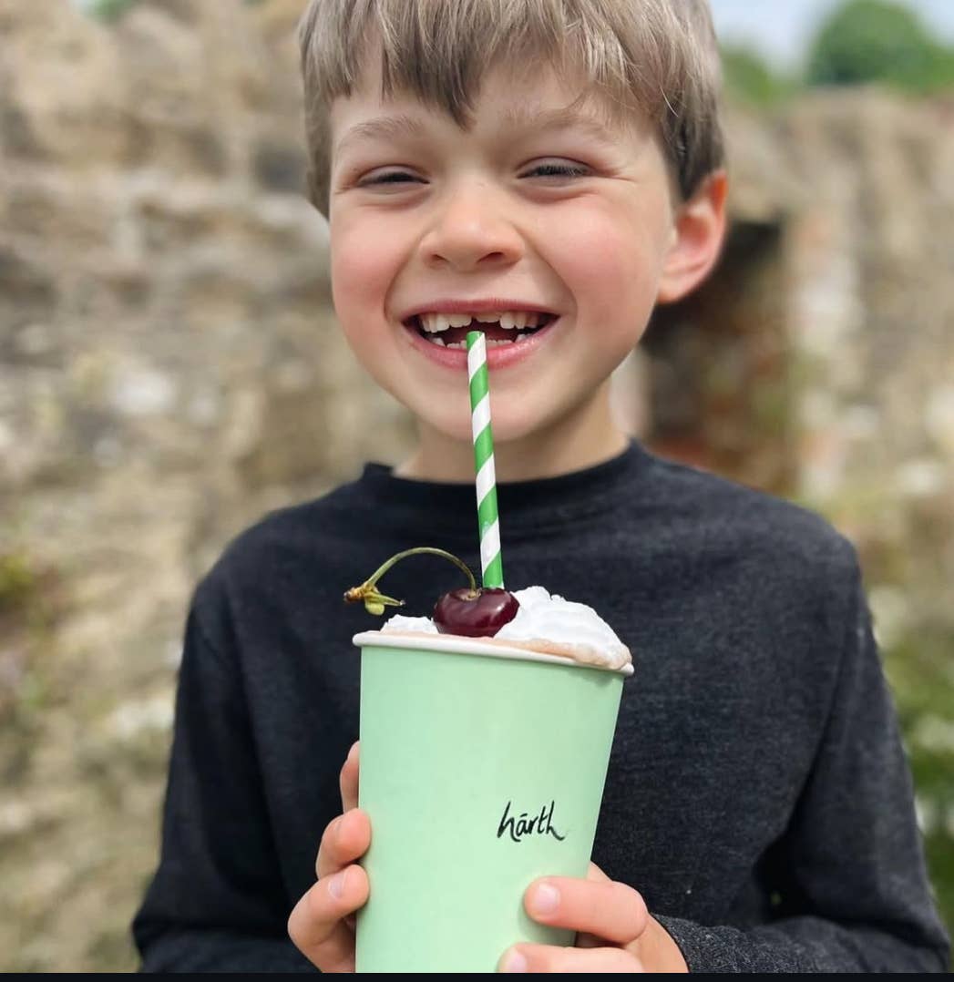 Child holding a mint green cup with a straw and cherry, outdoors.