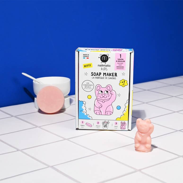 Soap maker packaging with a pink cat design on a tiled surface against a blue wall.