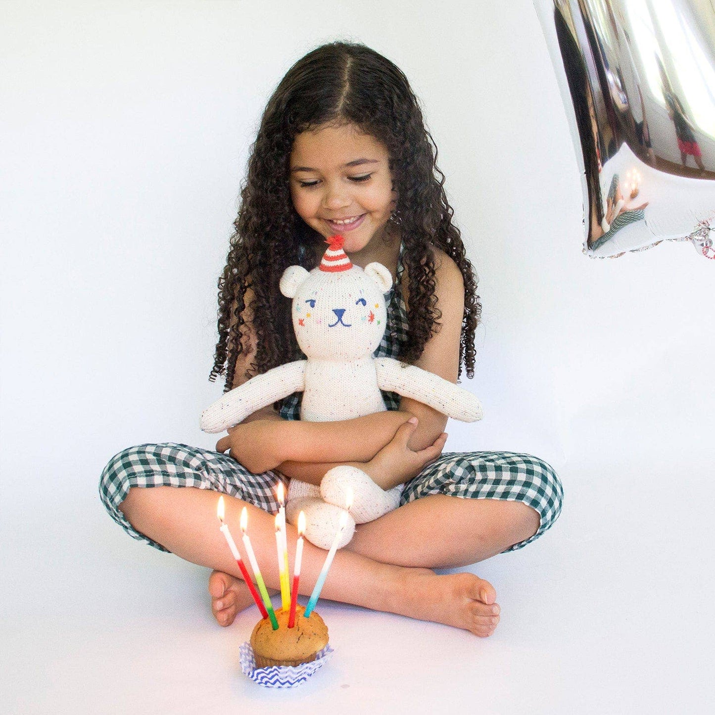 Child holding a teddy bear with a birthday cake and candles on a white background