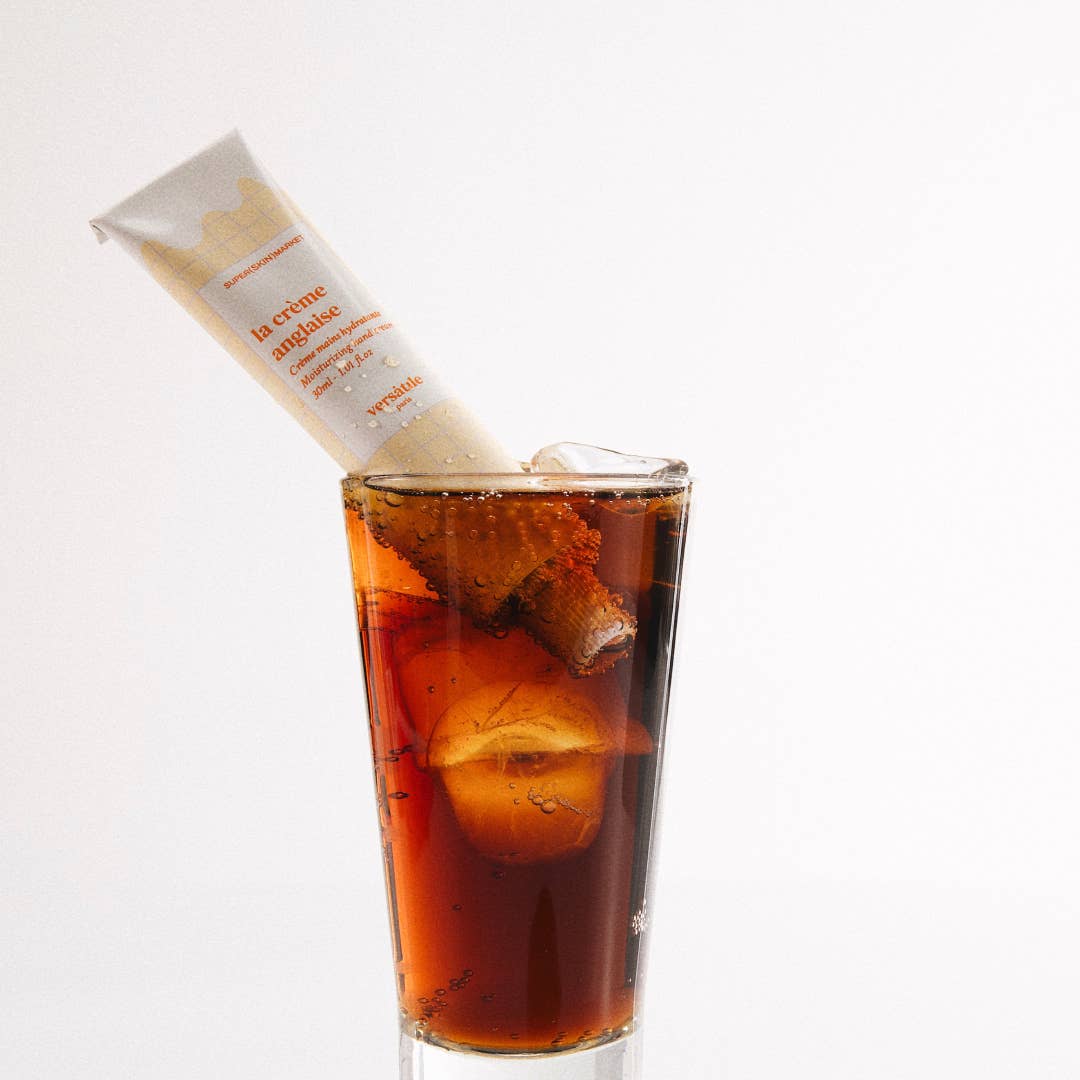 A glass of iced coffee with a hand cream tube placed upright on top, partially occluding the view of the drink.