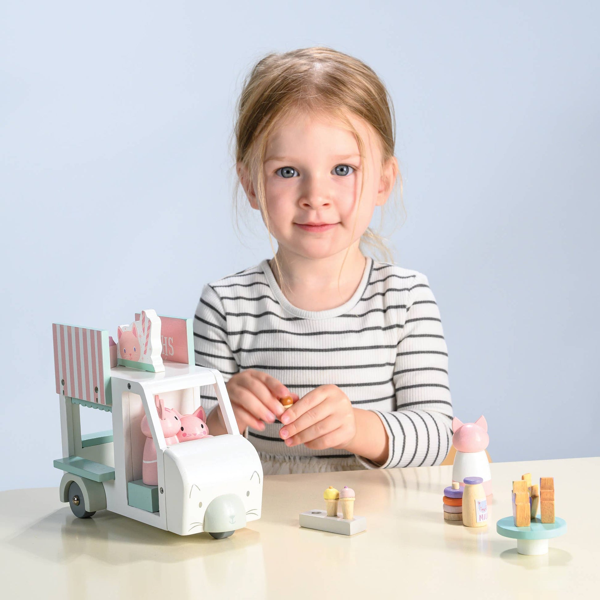 Child playing with a toy ice cream cart and figurines on a light surface with a light blue background