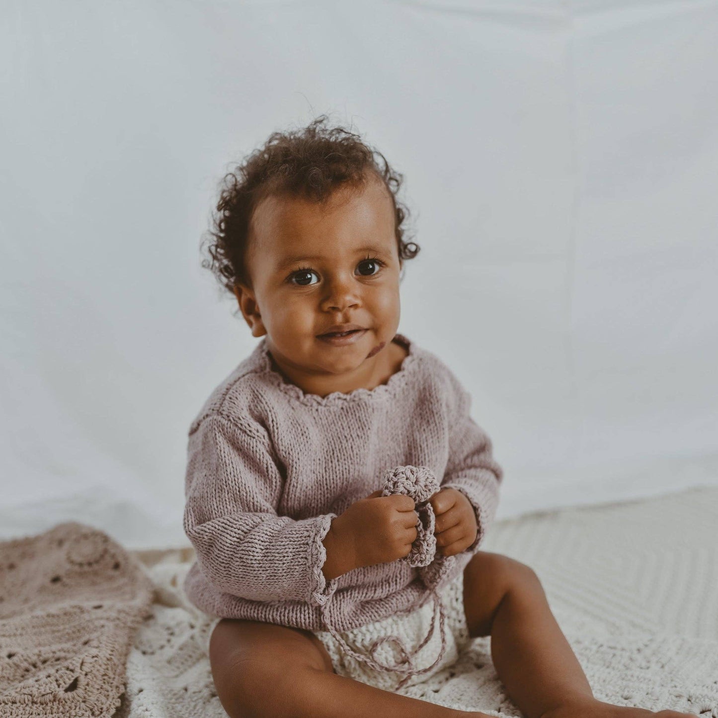 Baby in a pink outfit sitting on a white blanket with a textured background