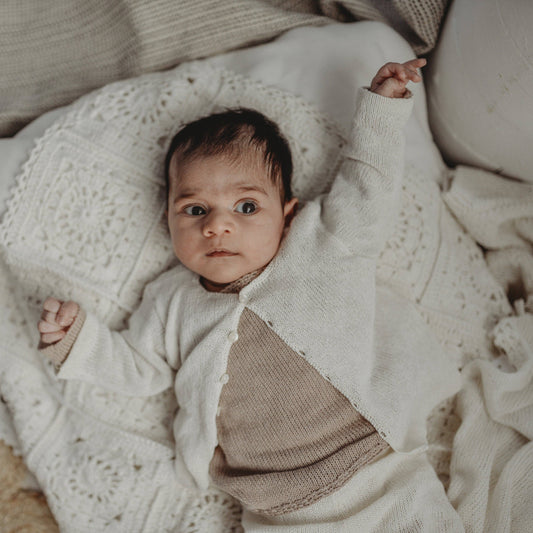 Baby wrapped in a white knit blanket with a neutral background