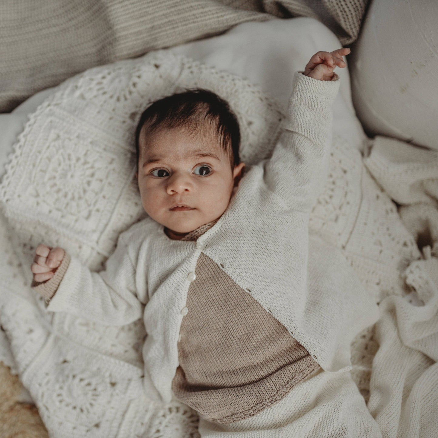Baby wrapped in a white knit blanket with a neutral background