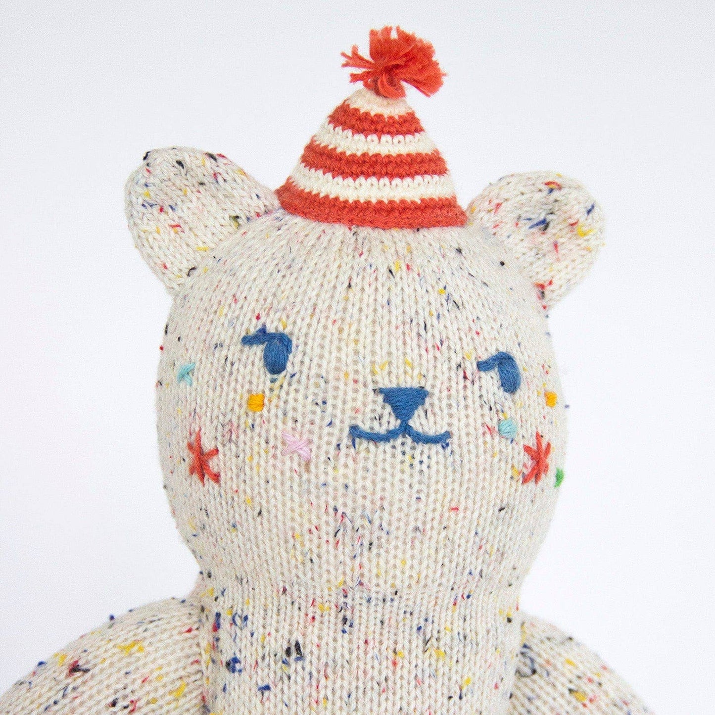 Knitted bear with colorful speckles and a striped red and white hat on a white background
