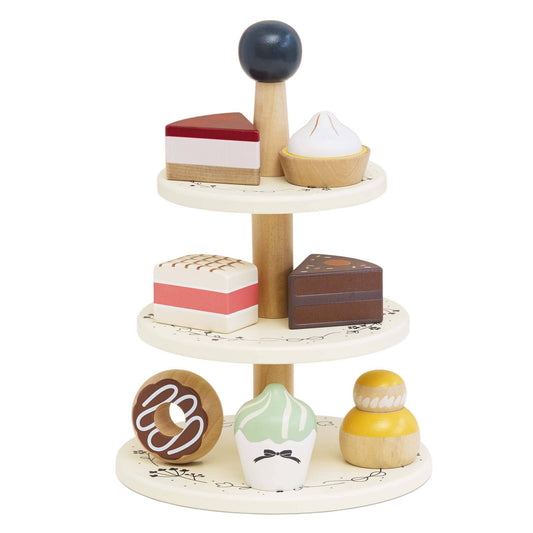 A wooden three-tier cake stand with various painted toy cakes and pastries on it, designed for pretend play.