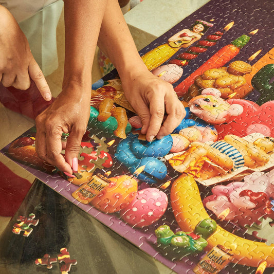 Person assembling a colorful puzzle with cartoonish food items on a table.