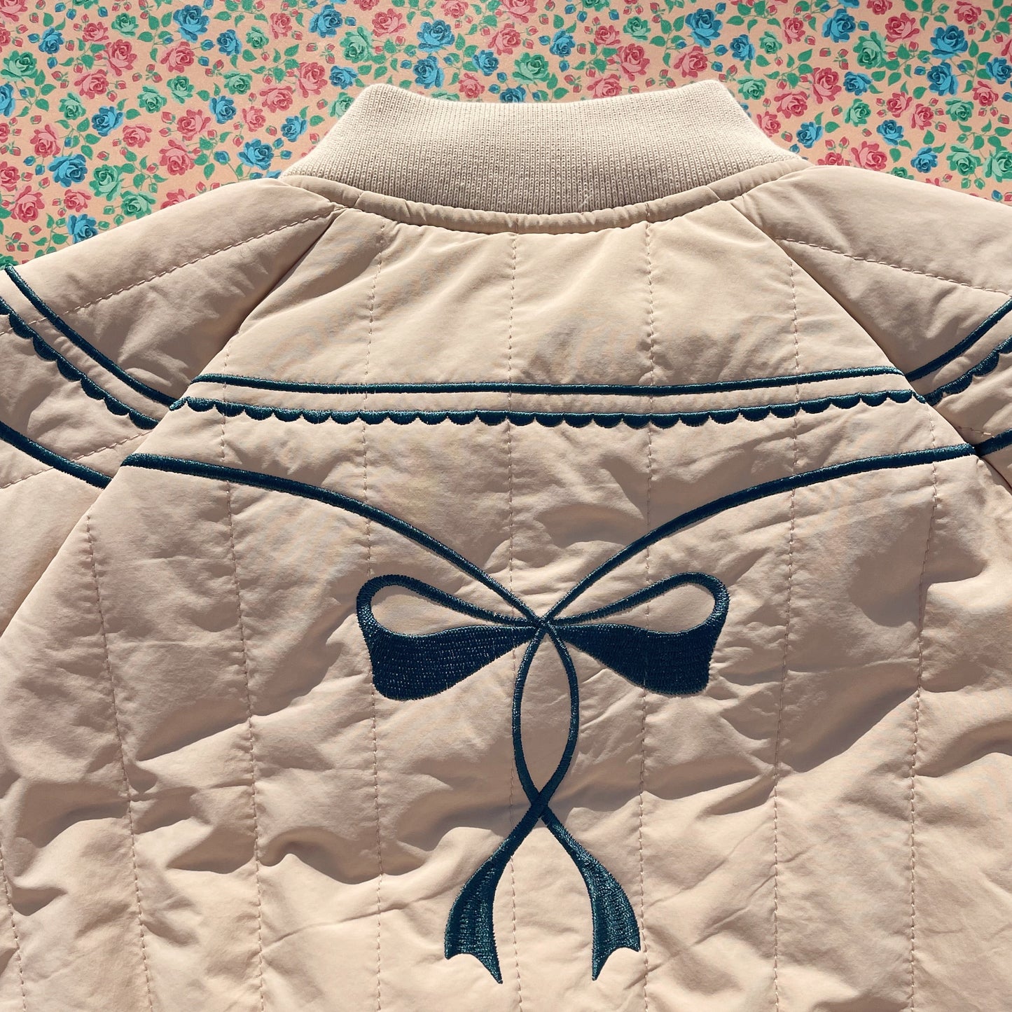 Beige quilted jacket with a blue bow design on a floral background