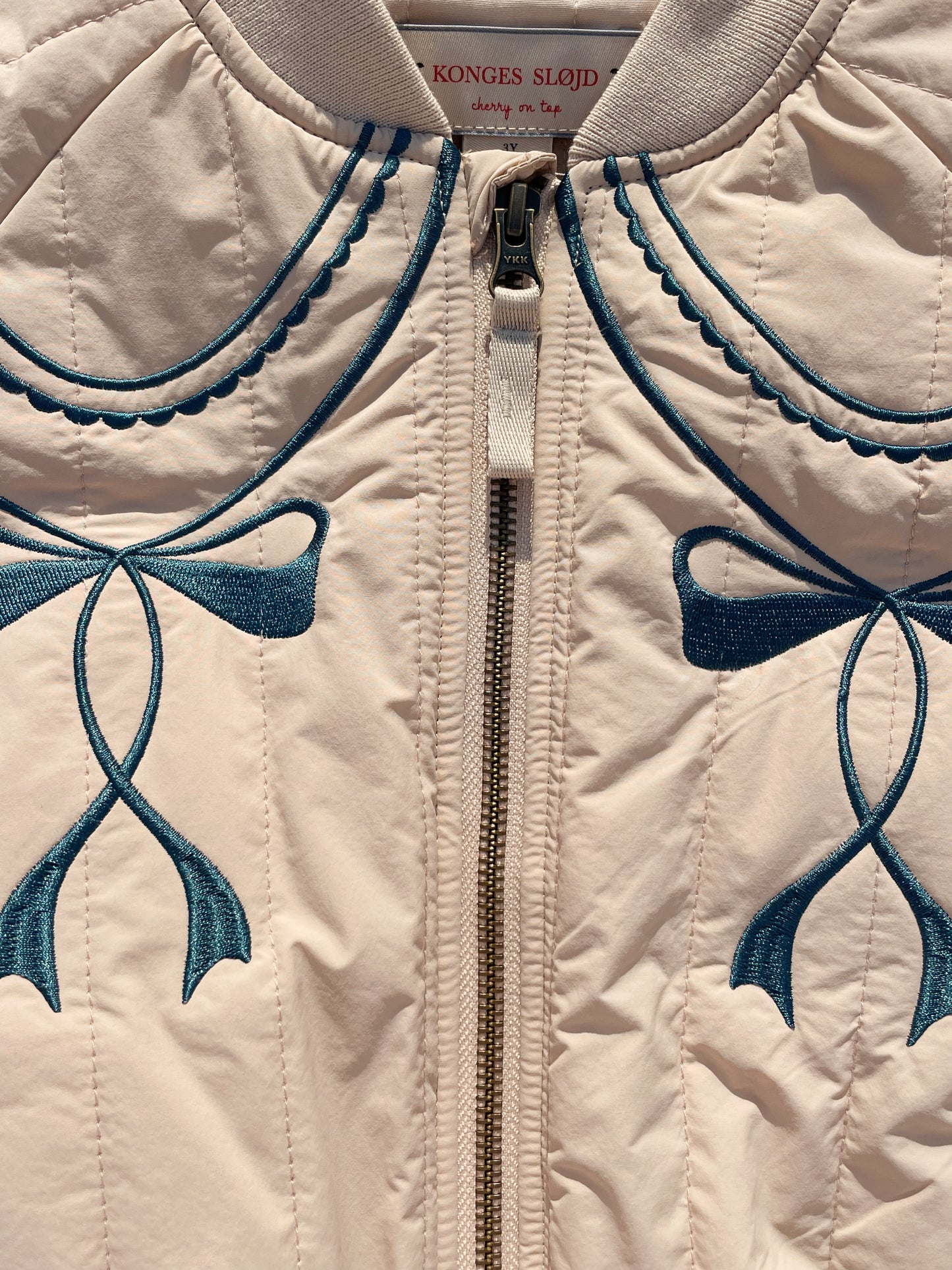 Close-up of a beige jacket with blue embroidery and a visible brand label.