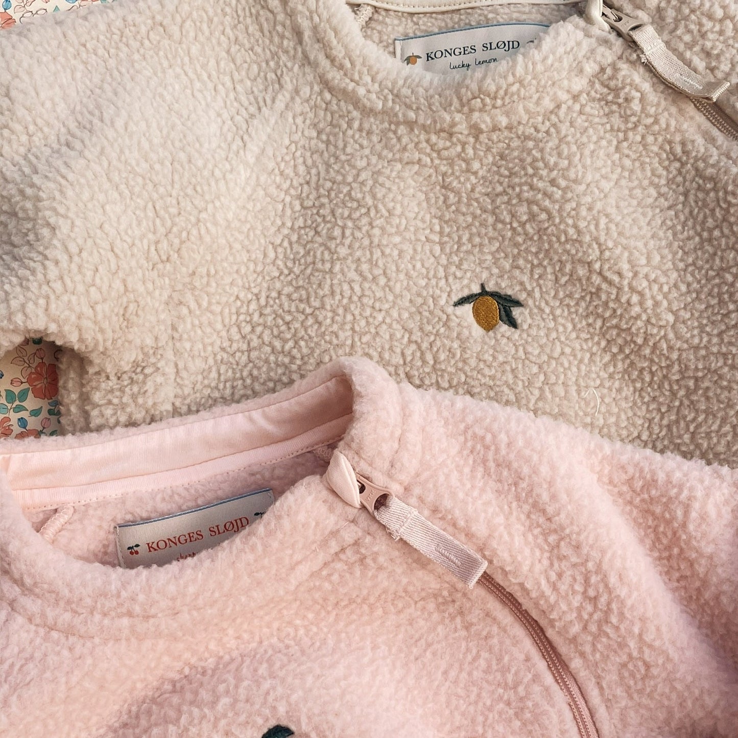 Close-up of two fleece jackets with embroidered designs on a neutral background