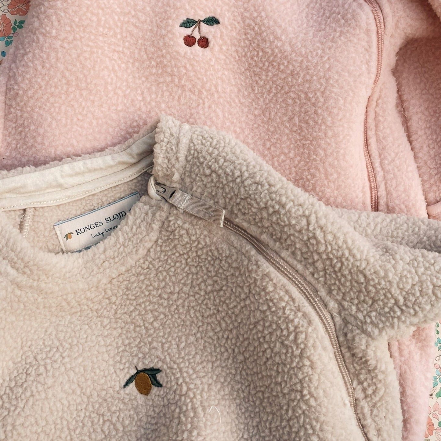 Two fleece jackets with embroidered designs on a floral background