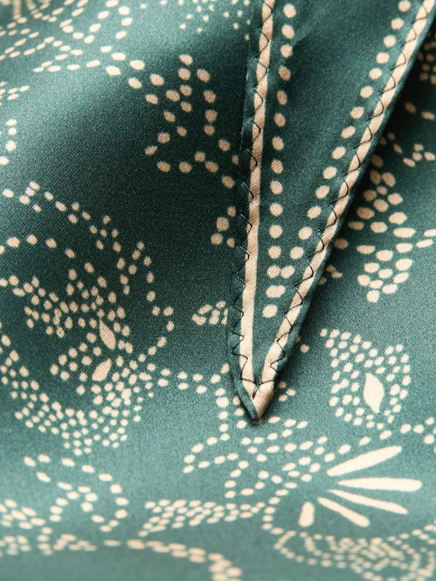 Close-up of green fabric with beige floral pattern and stitching detail