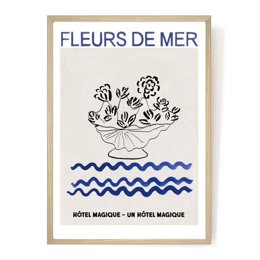 Hotel Magique Fleurs De Mers Print. The background is beige. The flowers and the flower pot is black. The waves below are dark blue in colour. “Fleurs De Mer” is written in dark blue. The print is framed.