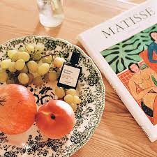 Plate of fruits with a bottle of perfume and a magazine on a wooden surface