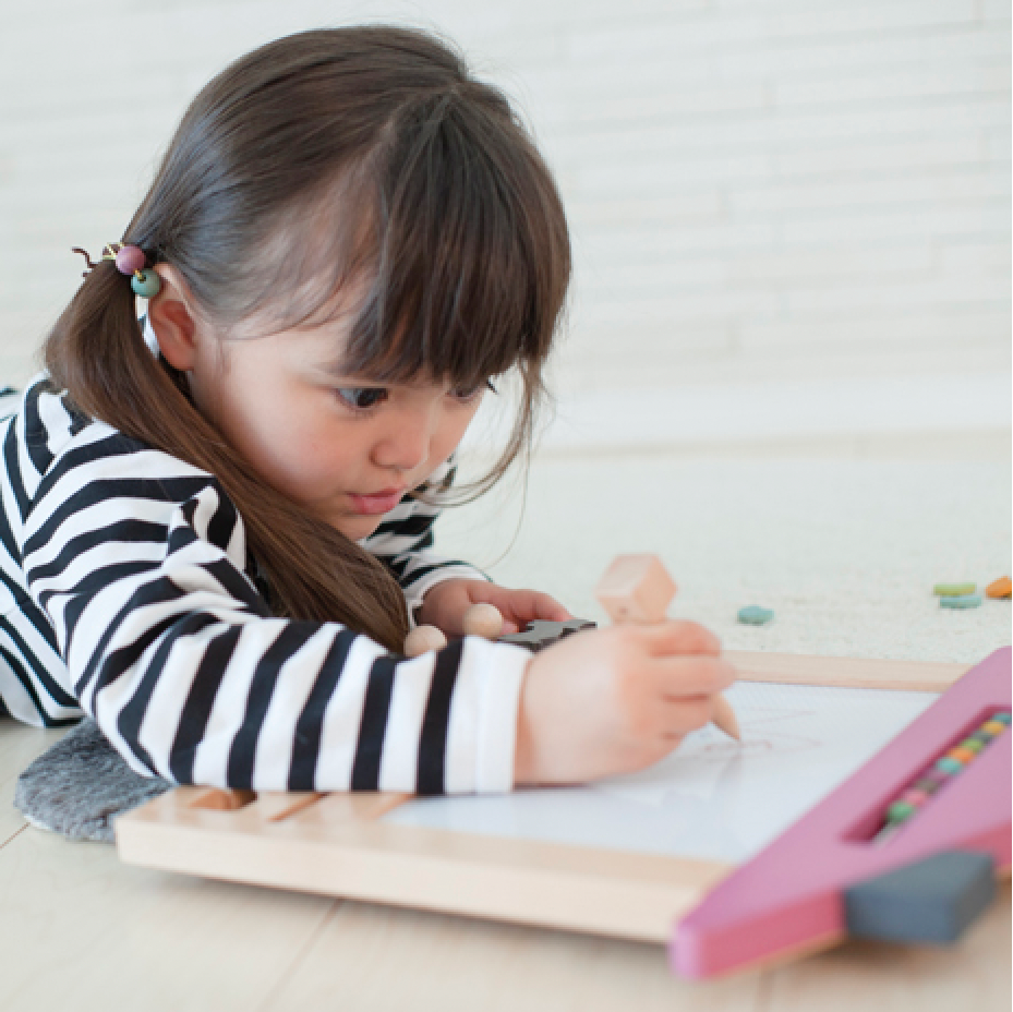 Child drawing on a piece of paper with a crayon on a light-colored floor.