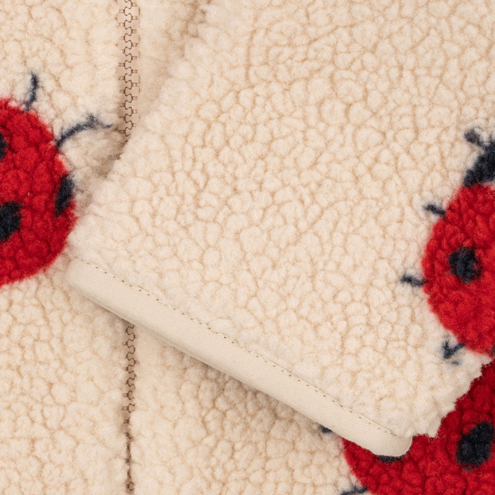 Close-up of the Konges Sløjd Jody Teddy onesie in Ladybug Sand, showing the plush sherpa texture, red ladybird print, and soft cuff detailing for comfort