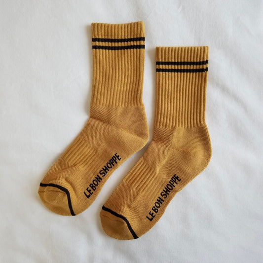 A pair of light brown ribbed crew socks with black stripe details, laid flat on a white fabric background, showing the Le Bon Shoppe branding on the sole and contrast toe accents.