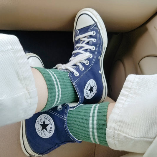 A close up of a person wearing green moss coloured ribbed crew socks with blue shoes while sitting in a car
