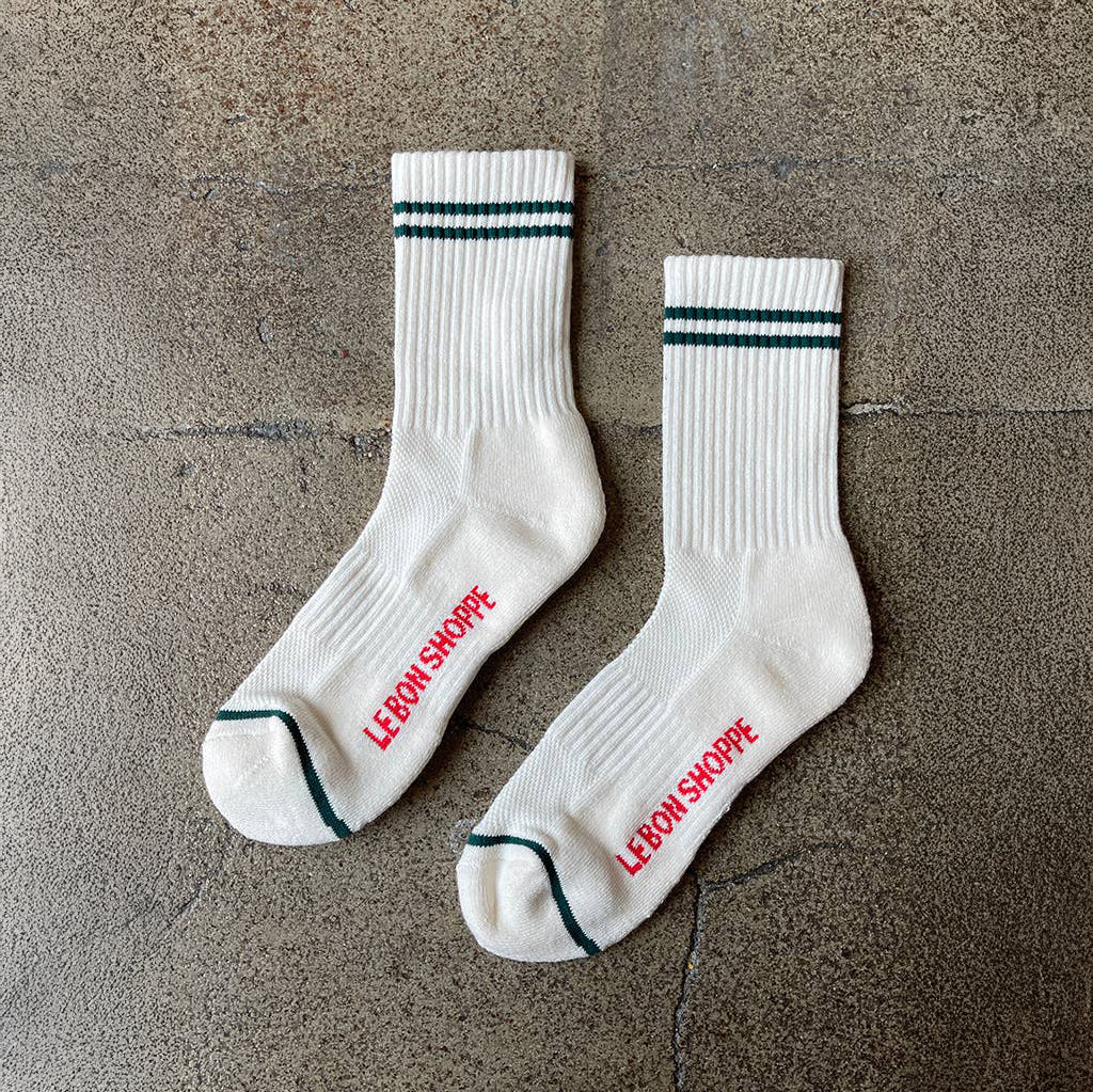 A pair of white Le Bon Shoppe Boyfriend Socks, featuring a white body with dark green bands around the top, and green toe accents.
